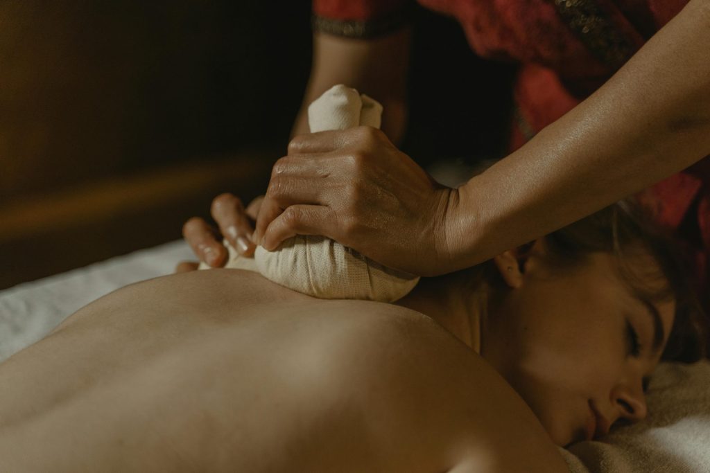 Nahaufnahme einer entspannenden Kräutermassage in einem schwach beleuchteten Spa-Ambiente.